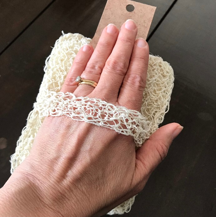 Biodegradable agave bath mitt with a hand in the back strap showing how it is used