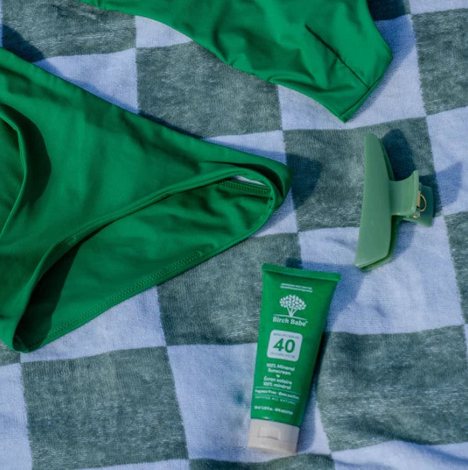 Birch Babe Mineral Sunscreen SPF 40 Fragrance Free on beach towel beside green swimwear – eco-friendly mineral sunscreen in compostable tube.