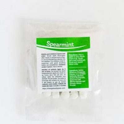 Close-up of spearmint-flavored toothpaste tablets in clear blister packaging, highlighting textured surface and round shape.