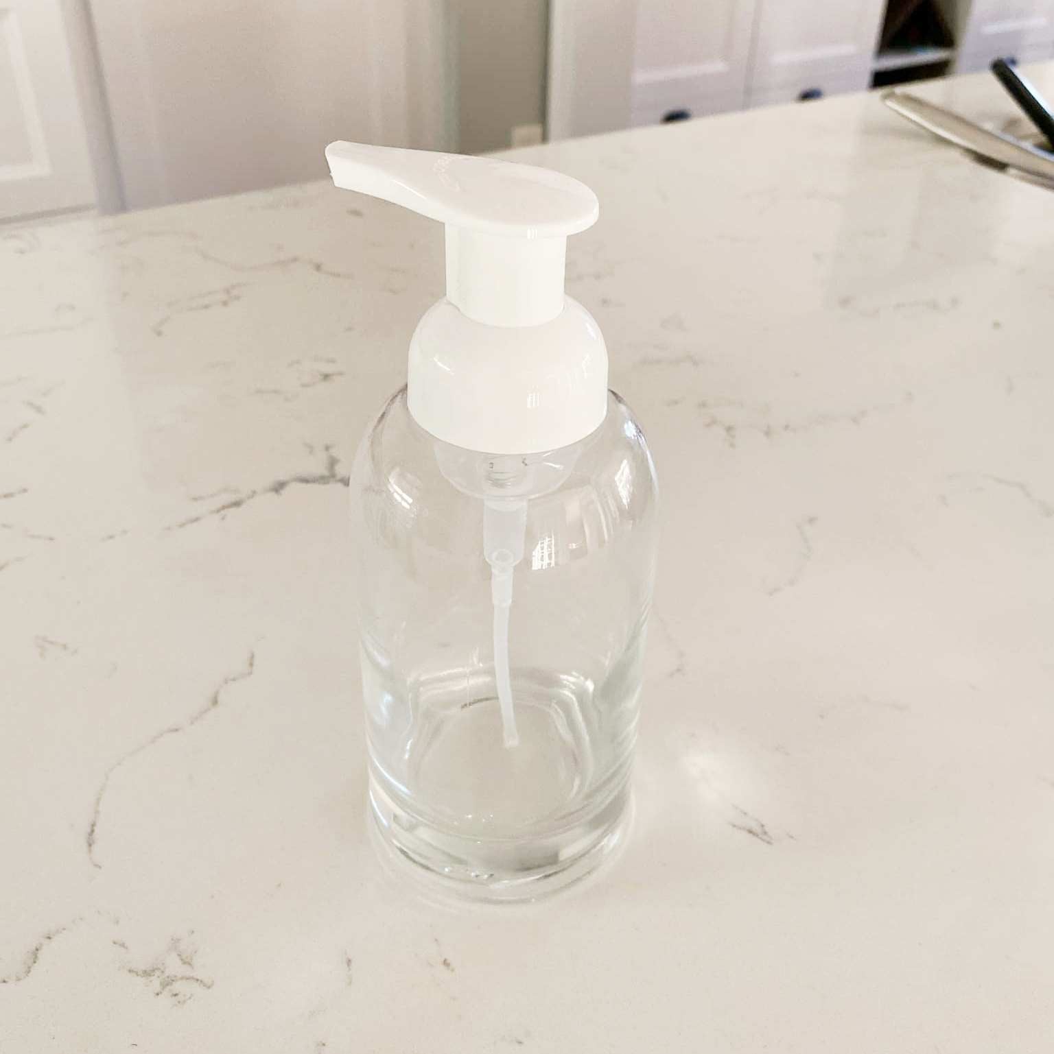 Close-up of the transparent glass bottle neck with a white pump dispenser and smooth textured surface, showing refill label