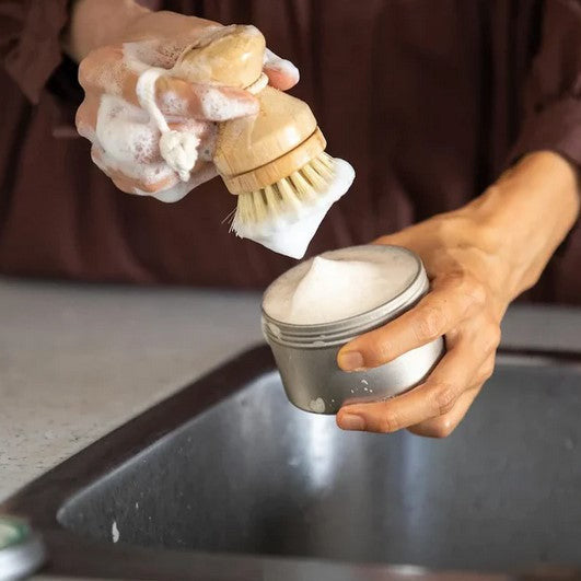 Close-up of the textured surface and rounded edges of the solid dish soap cake resting on a wooden dish brush holder.