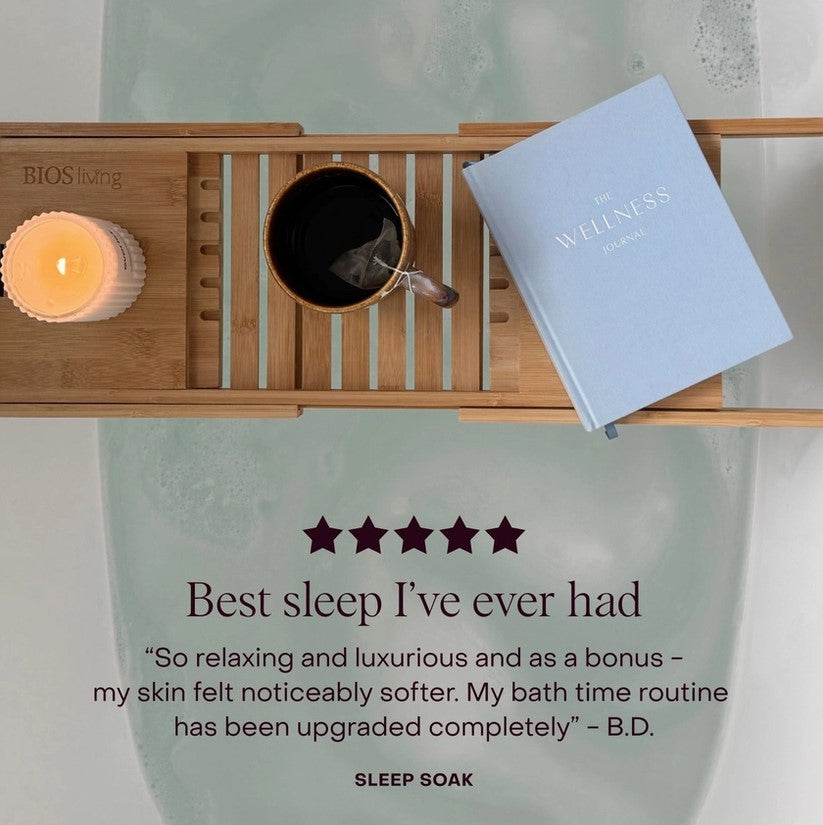Bath tray with candle, mug, and book on a green background with review about the sleep soak product.
