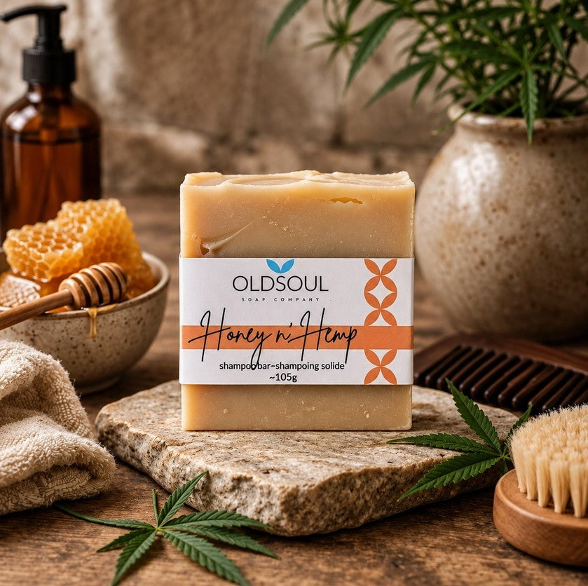 Old Soul Soap Company Honey n’ Hemp Shampoo Bar, 105g, displayed with honeycomb, a wooden honey dipper, hemp leaves and natural bath accessories in a rustic setting.
