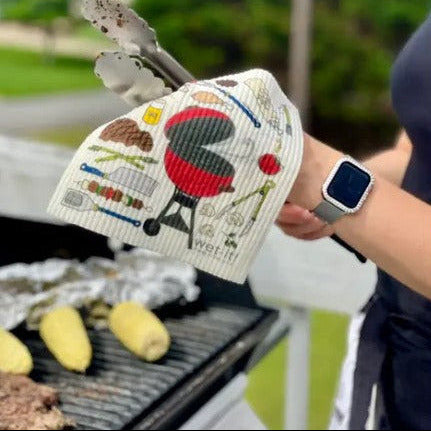 Wet-It Swedish dishcloth barbecue pattern being used outdoors near grill, eco-friendly reusable cleaning cloth for kitchen and BBQ cleanup
