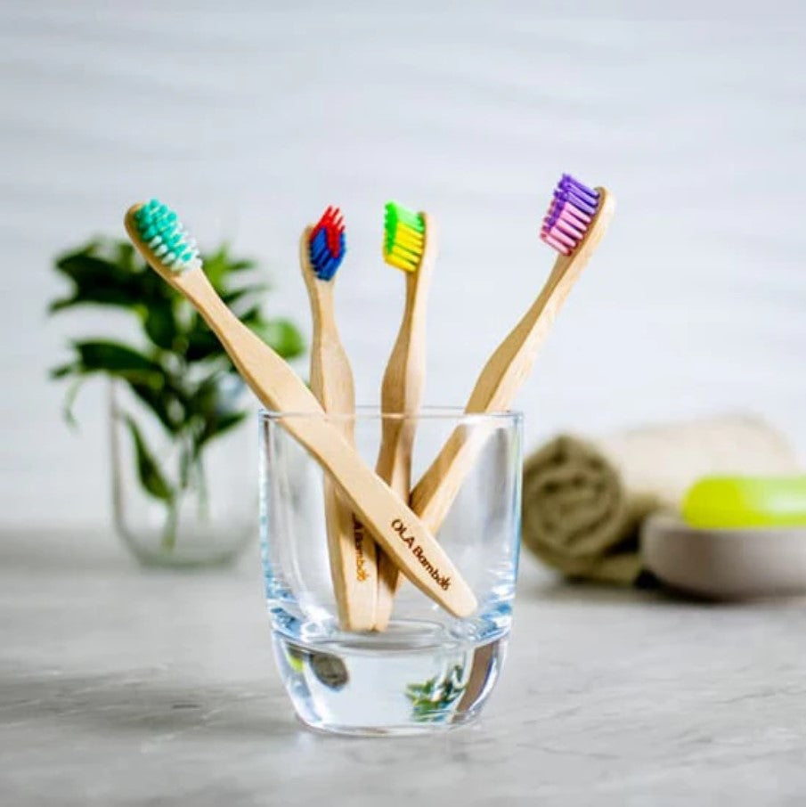 Close-up of four colorful bamboo toothbrush bristles in different shades of green, blue, pink, and yellow showing textured
