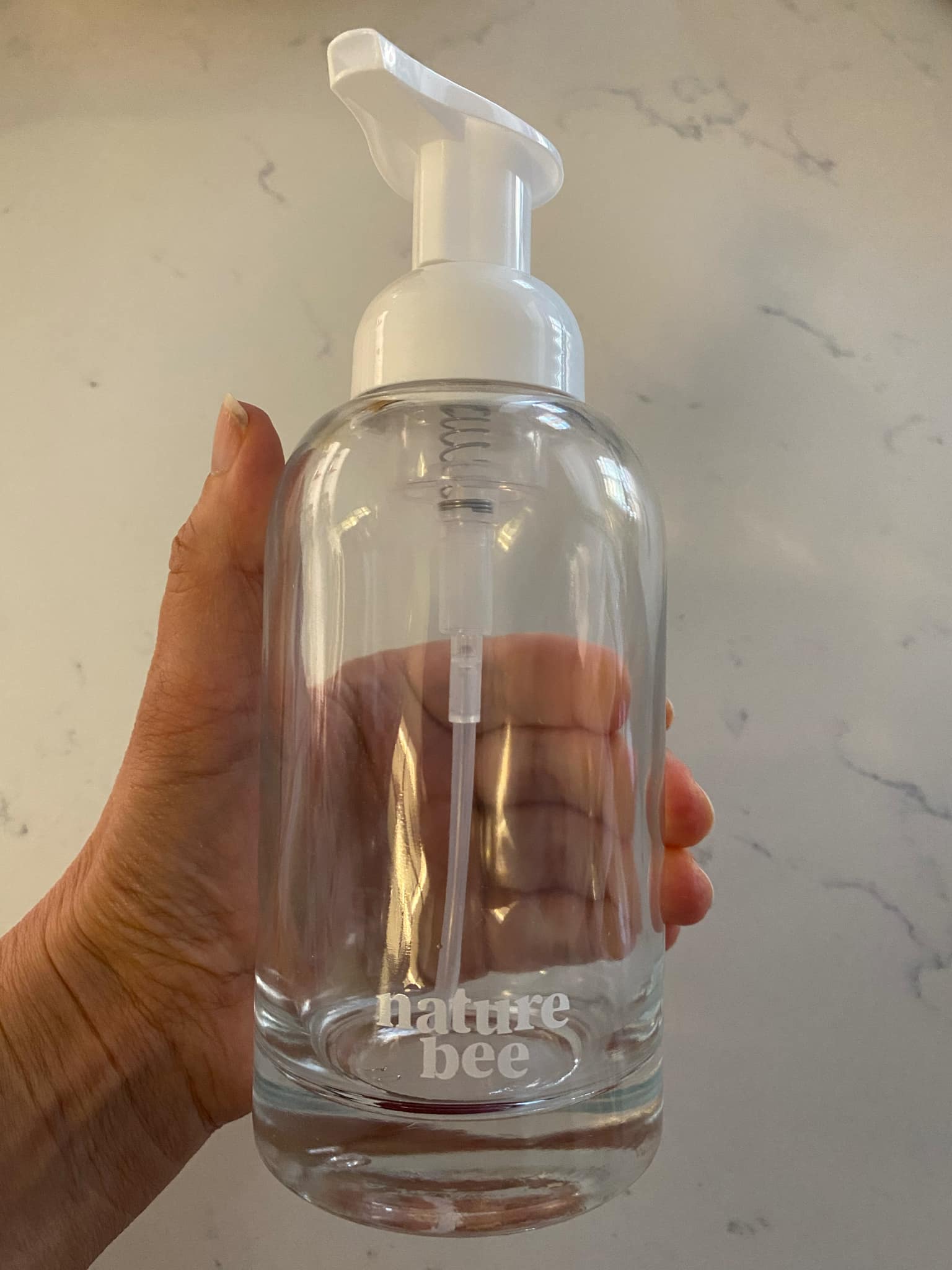 Close-up of the clear glass refillable soap bottle’s textured pump top with a white foaming soap discharge visible