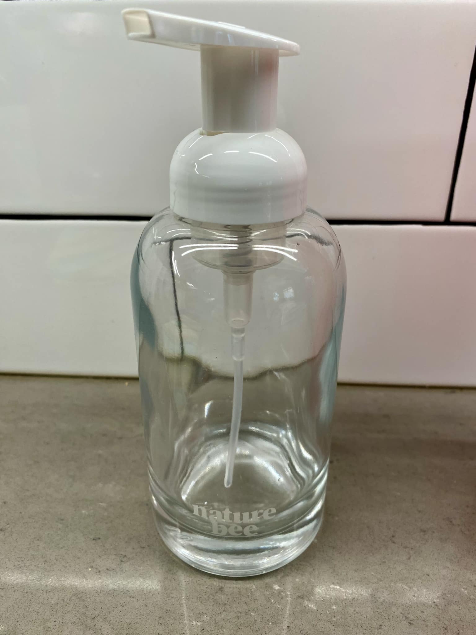 Close-up of the clear glass foam dispenser with a white pump and a textured label reading "Nature Bee" in black lettering.