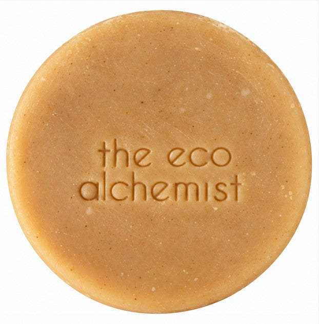 A round, light brown bar of soap with the words 'the eco alchemist' embossed in the center, shown against a plain white background.