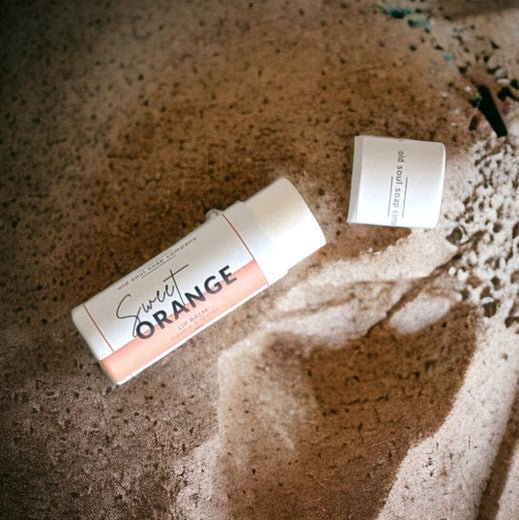 Close-up of the Sweet Orange Lip Balm tube showing textured orange label and shiny silver cap detail