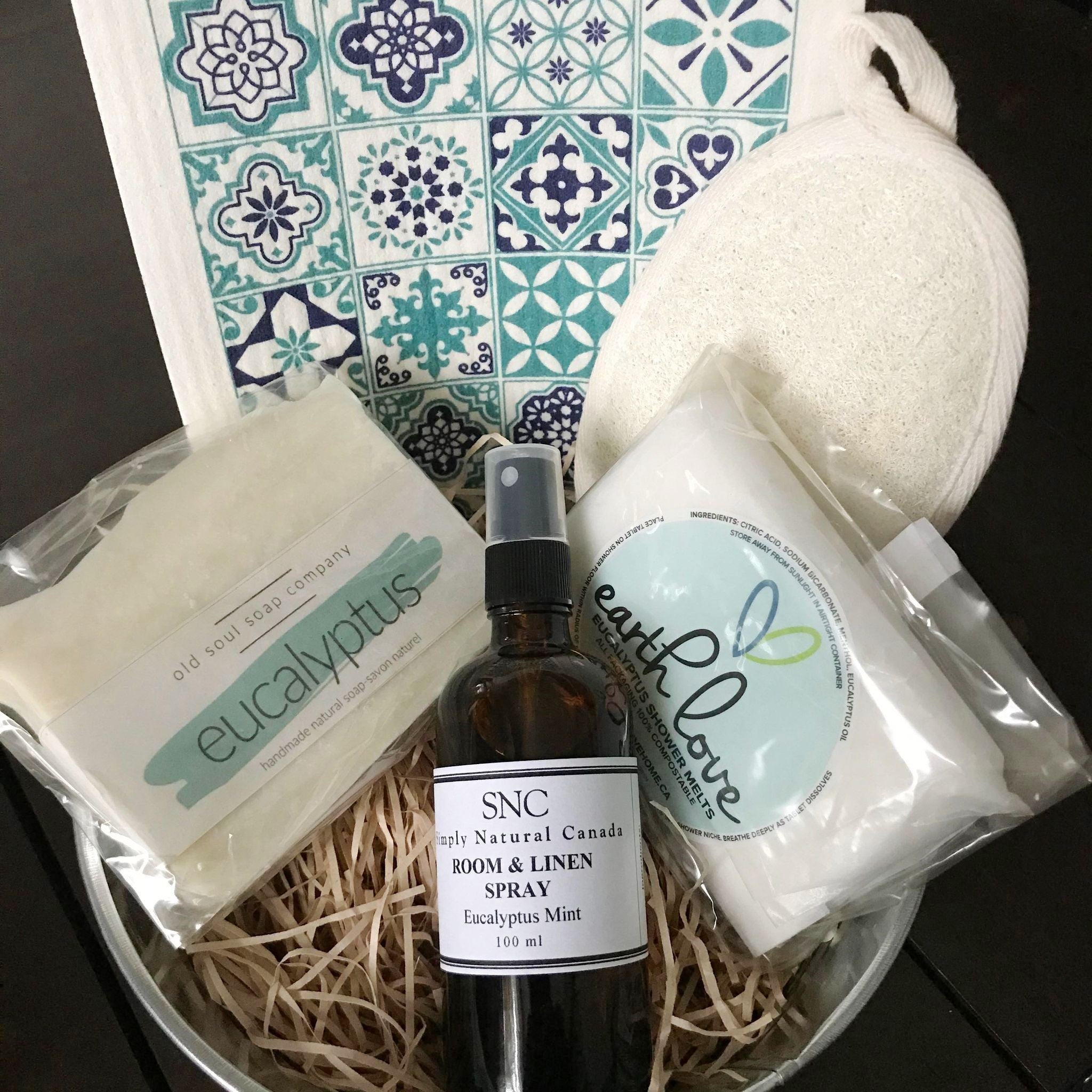 Eucalyptus spa gift basket with pastel green towel, eucalyptus branch, glass jar with bath salts, and soy candle from