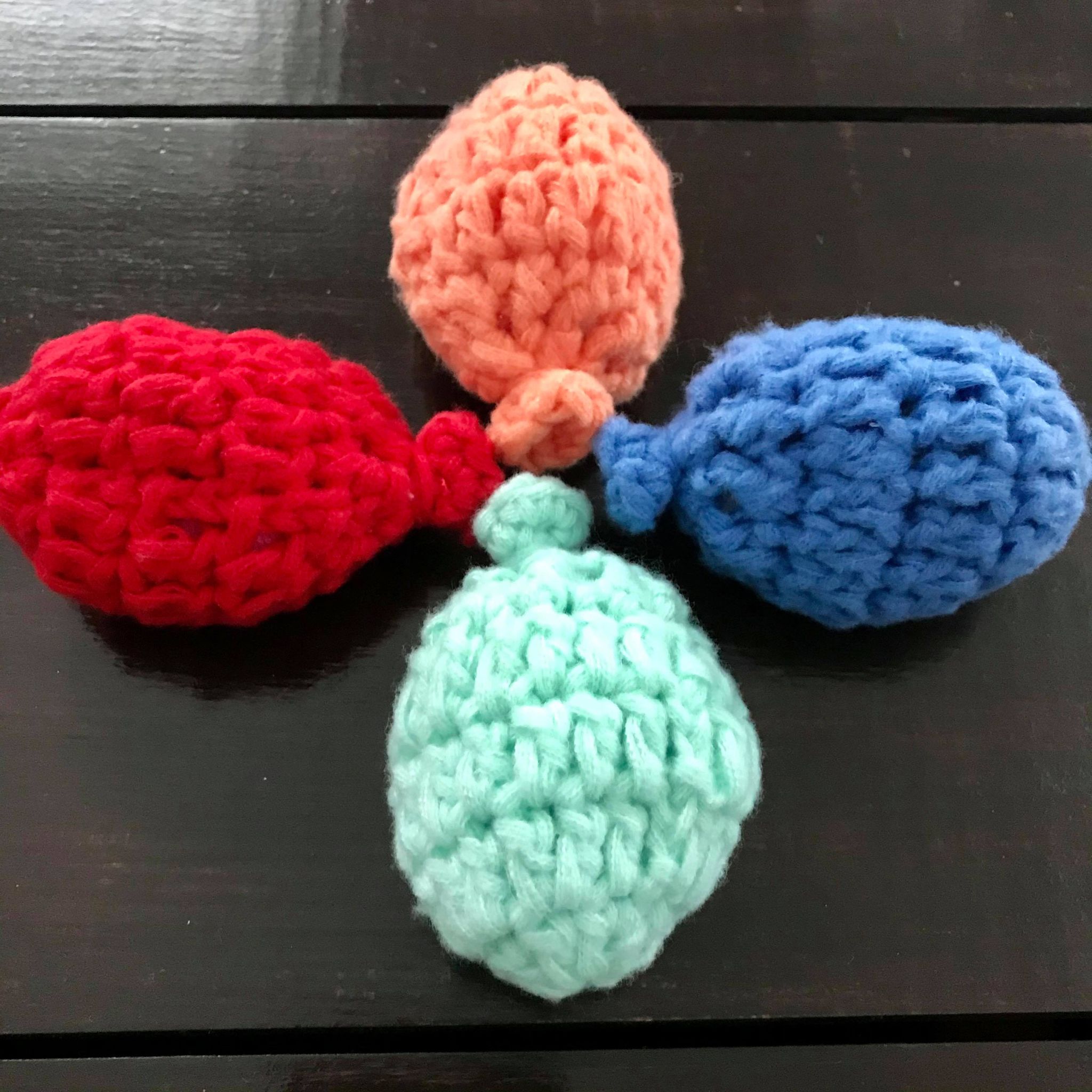 Close-up of crocheted water balloons revealing textured, multicolored yarn stitches and small dangling water-filled pouches.