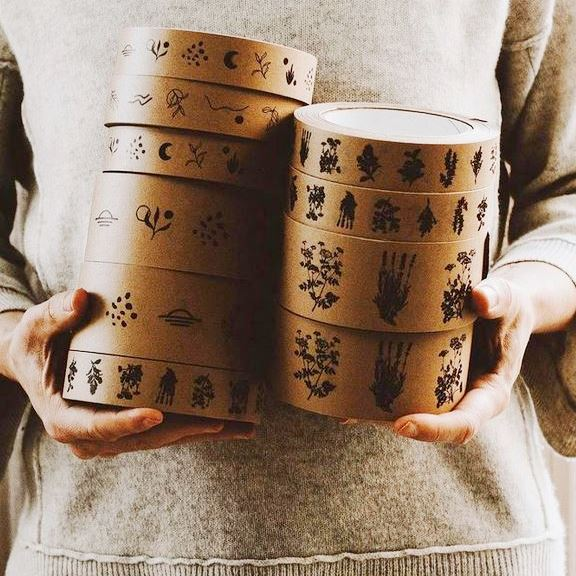 A woman holding two stacks of brown herbal themed decorative paper tape in 25 mm and 50 mm widths