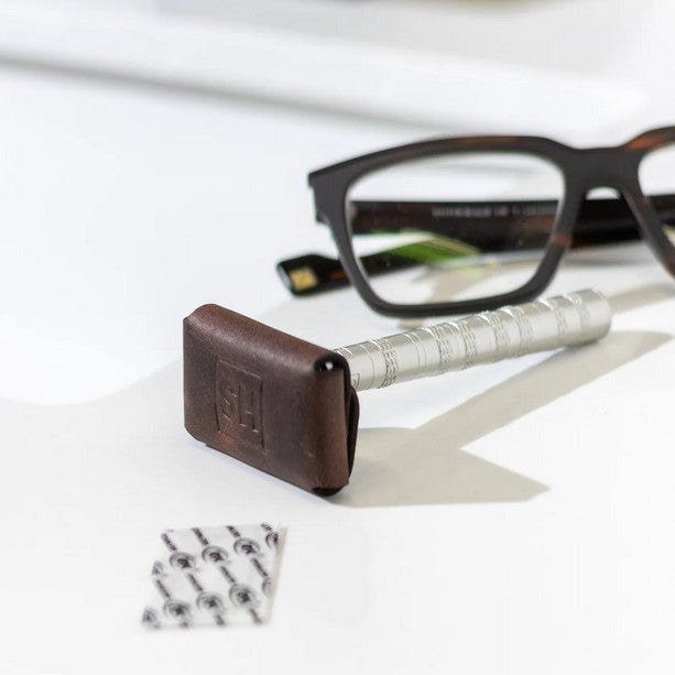 Henson Razor with brown leather head cover resting on counter beside eyeglasses
