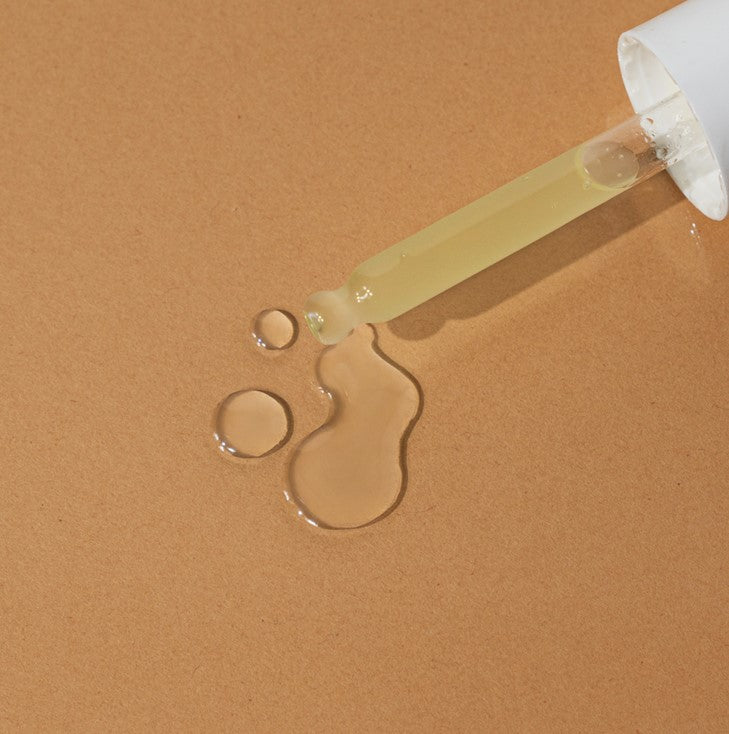 Close-up of the Natural Glow Face Serum bottle neck highlighting the soft, floral-scented serum flowing onto fingertips in a