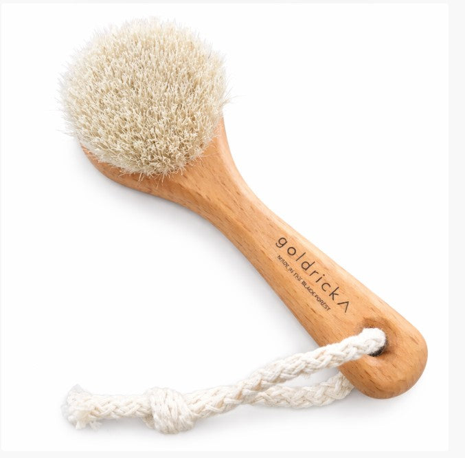 Close-up of the small face brush with wooden handle ideal for gentle facial exfoliation on a white background