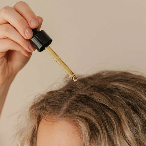 Applying Good Juju Hair Elixir to scalp with dropper for hydration and scalp care