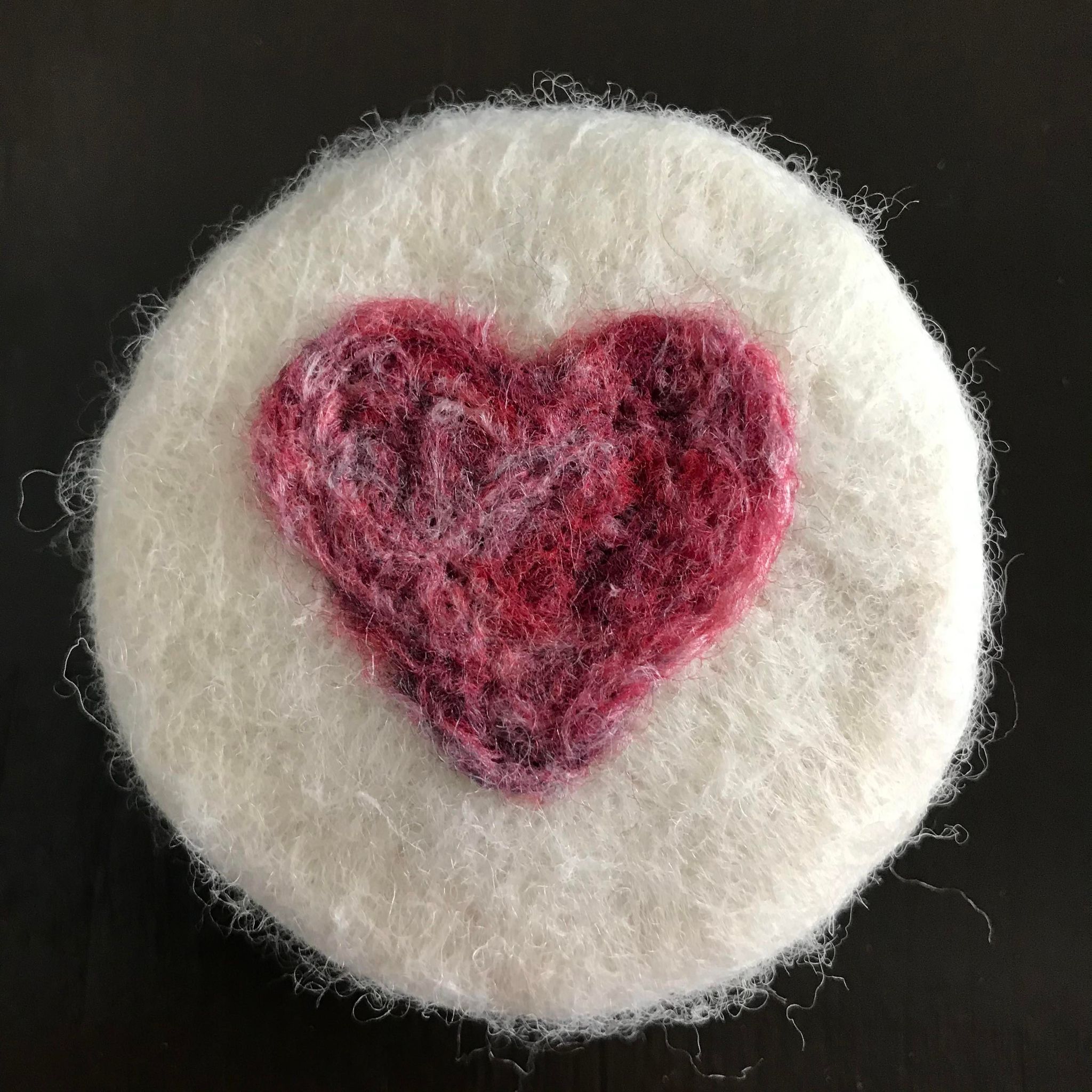 Close-up of felted soap’s textured surface showcasing vibrant red and pink wool fibers intertwined with soft grey accents.