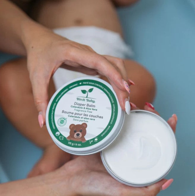 Cracked open jar of Birch Baby Diaper Balm revealing a smooth, creamy texture and natural soothing ingredients, ready for