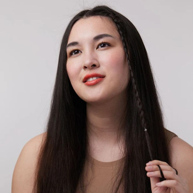 Close-up of the Sunset Seeker Lip and Cheek Tint tube showing vibrant coral shade and matte finish, with textured applicator