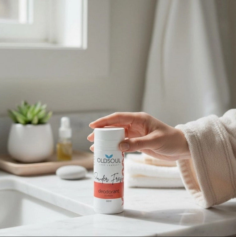 Hand holding Powder Fresh Natural Deodorant by The Old Soul Soap Company, a Canadian-made aluminum-free deodorant scented with vanilla and rose, styled in a bright bathroom setting.