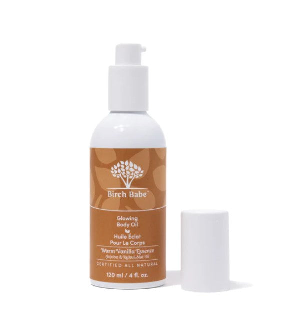 Birch Babe Glowing Body Oil in a clear glass bottle with warm vanilla-colored liquid and white pump spray cap, labeled "Warm