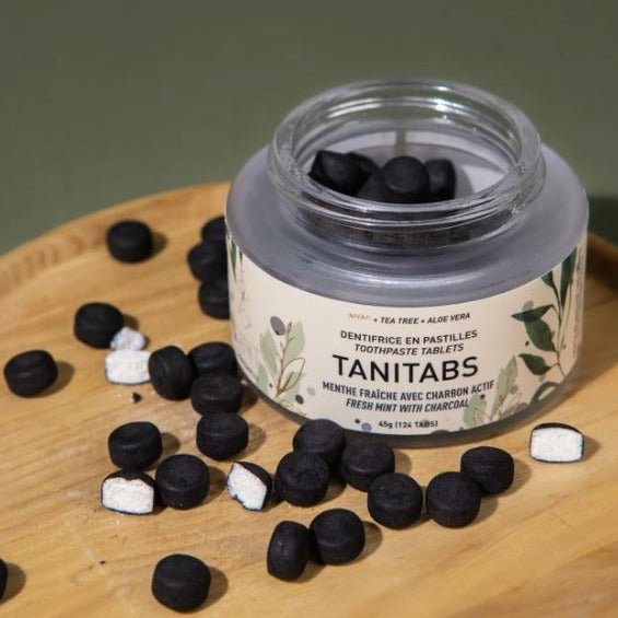 Close-up of the rounded mint-flavored charcoal toothpaste tablets inside a transparent glass jar, showcasing their smooth