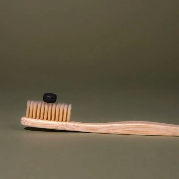 Close-up of activated charcoal tablets inside clear container, showing textured surface and mint scent beads for fresh