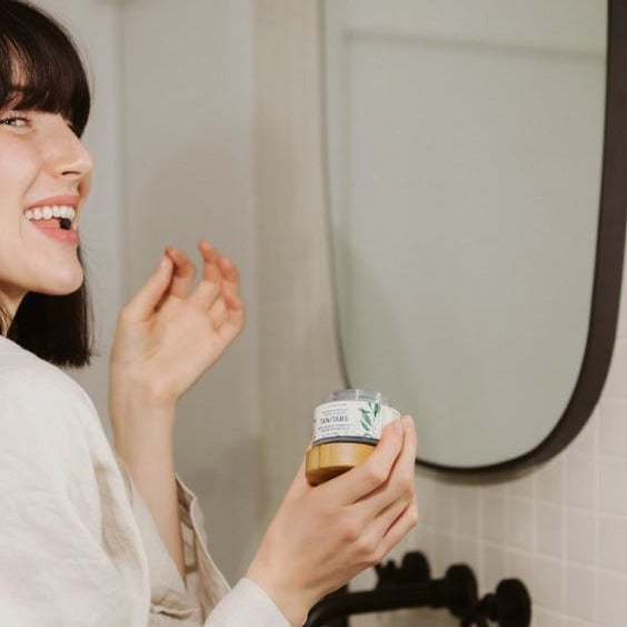 Close-up of activated charcoal and mint tablets inside clear glass jar showing textured surface and sample for oral