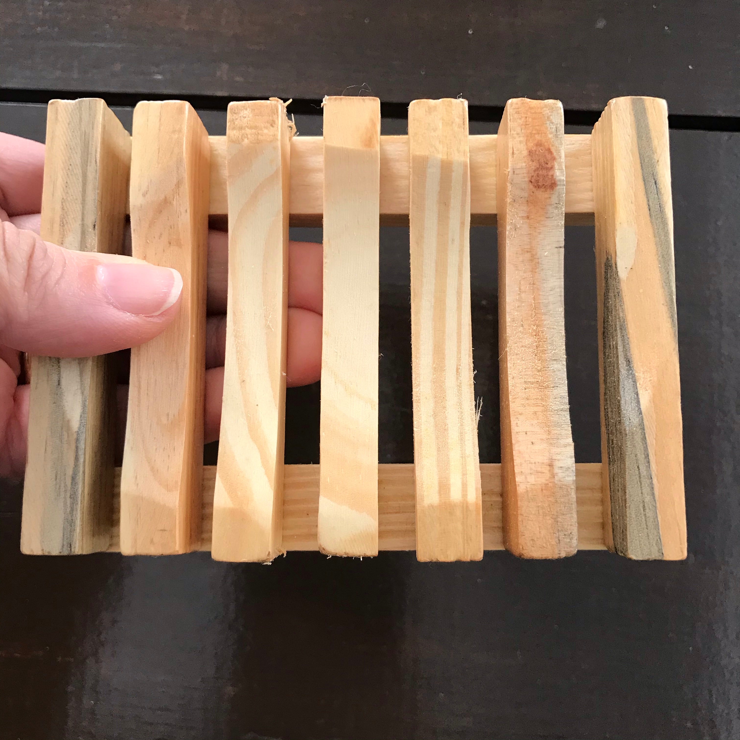 Close-up of slatted wood soap dish showing textured surface and rounded edges from a top-front angle.