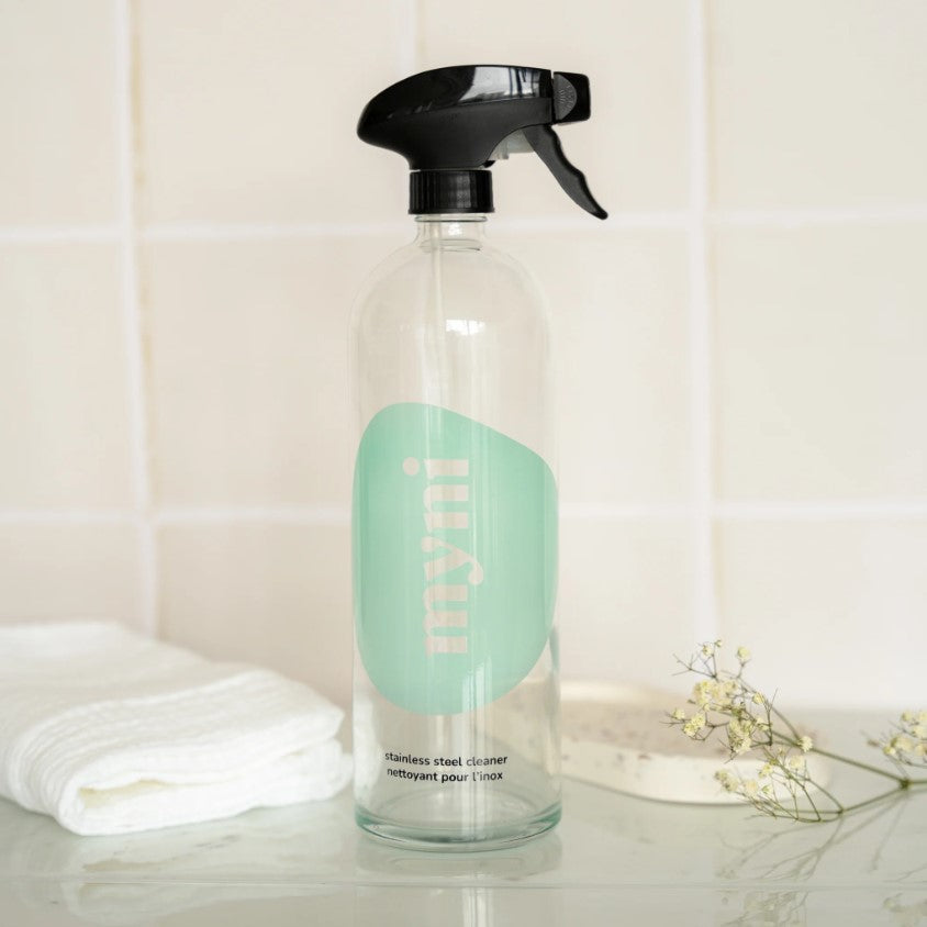 Close-up of the clear glass spray bottle neck with textured pump detail and minimalist white label positioned on a wooden